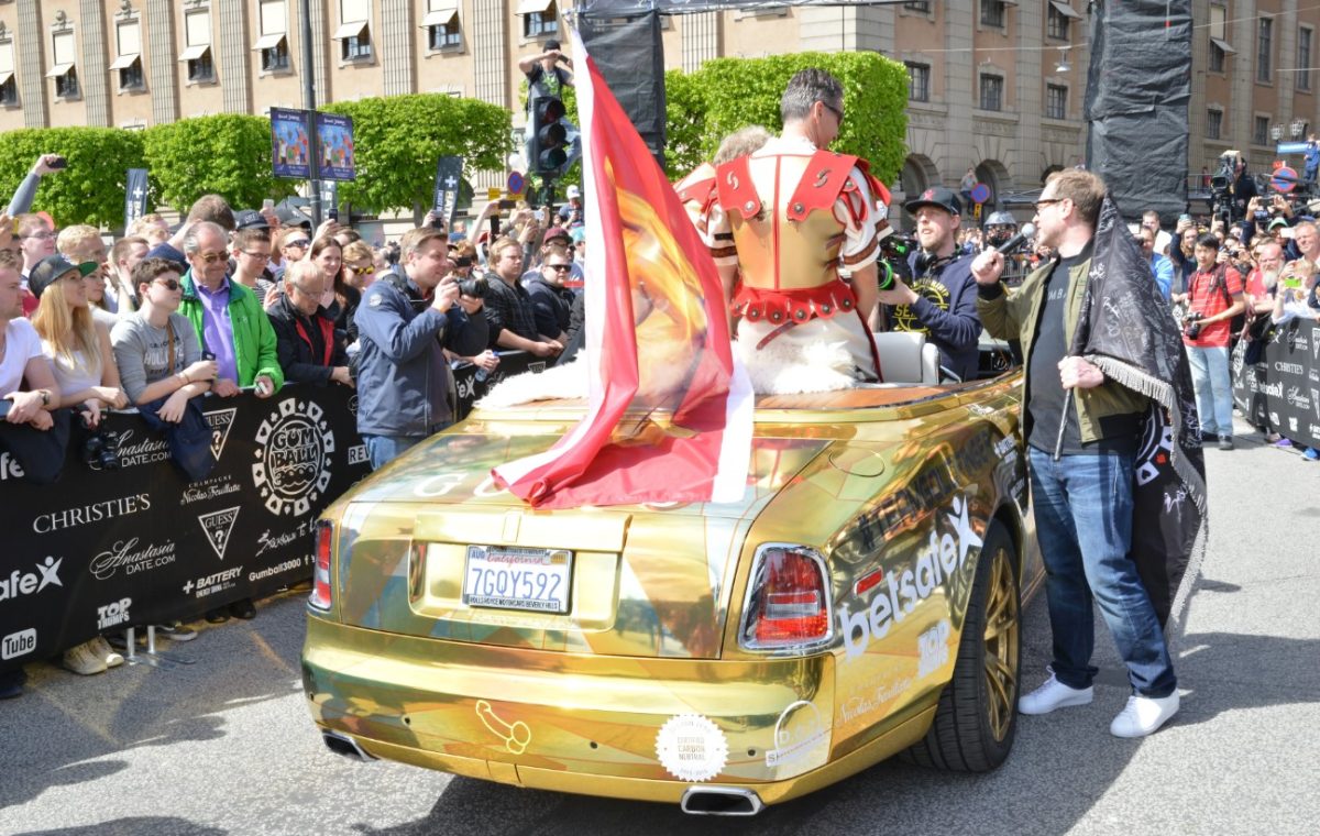 A man dressed as a Roman emperor drives a gold Rolls-Royce.